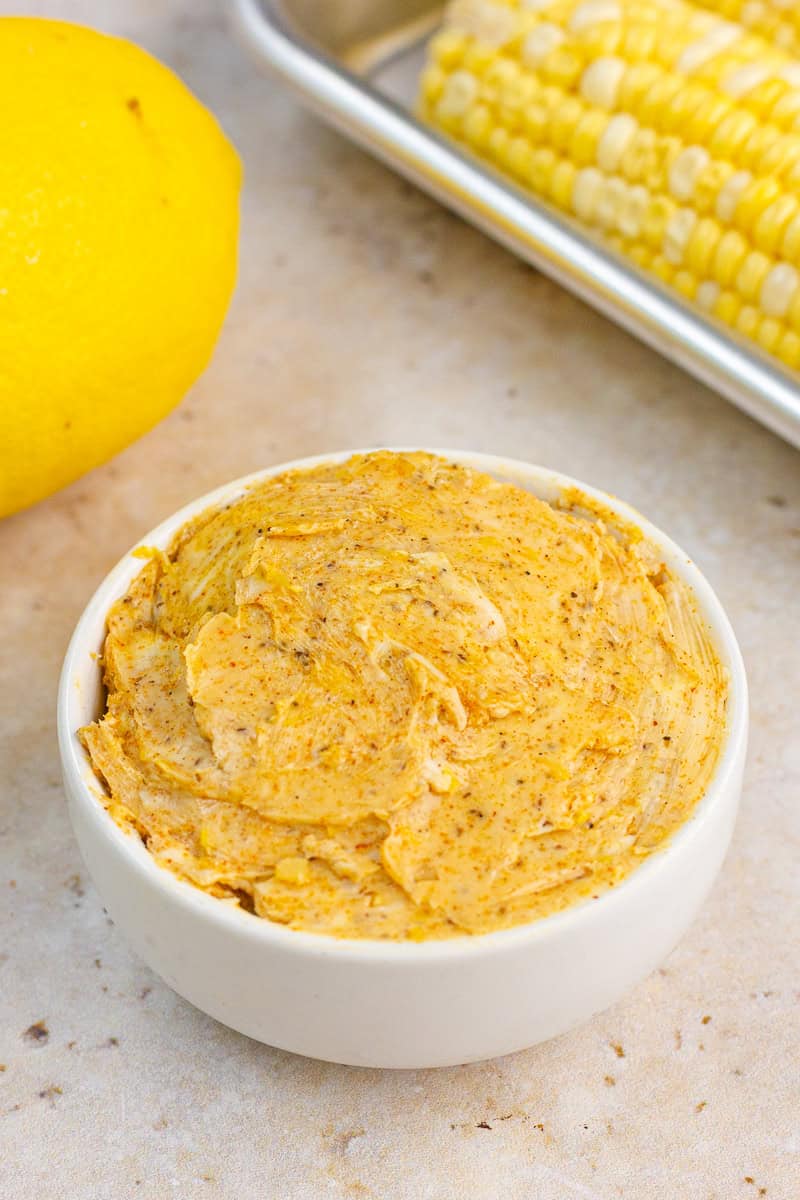 A bowl of Old Bay butter sits beside a lemon and fresh corn on the cob.