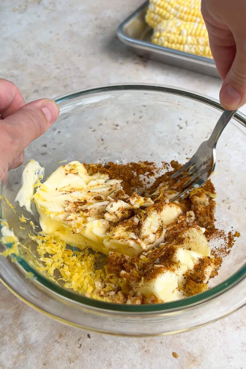 Old Bay seasoning, garlic, lemon zest, and softened butter are mixed in a glass bowl.