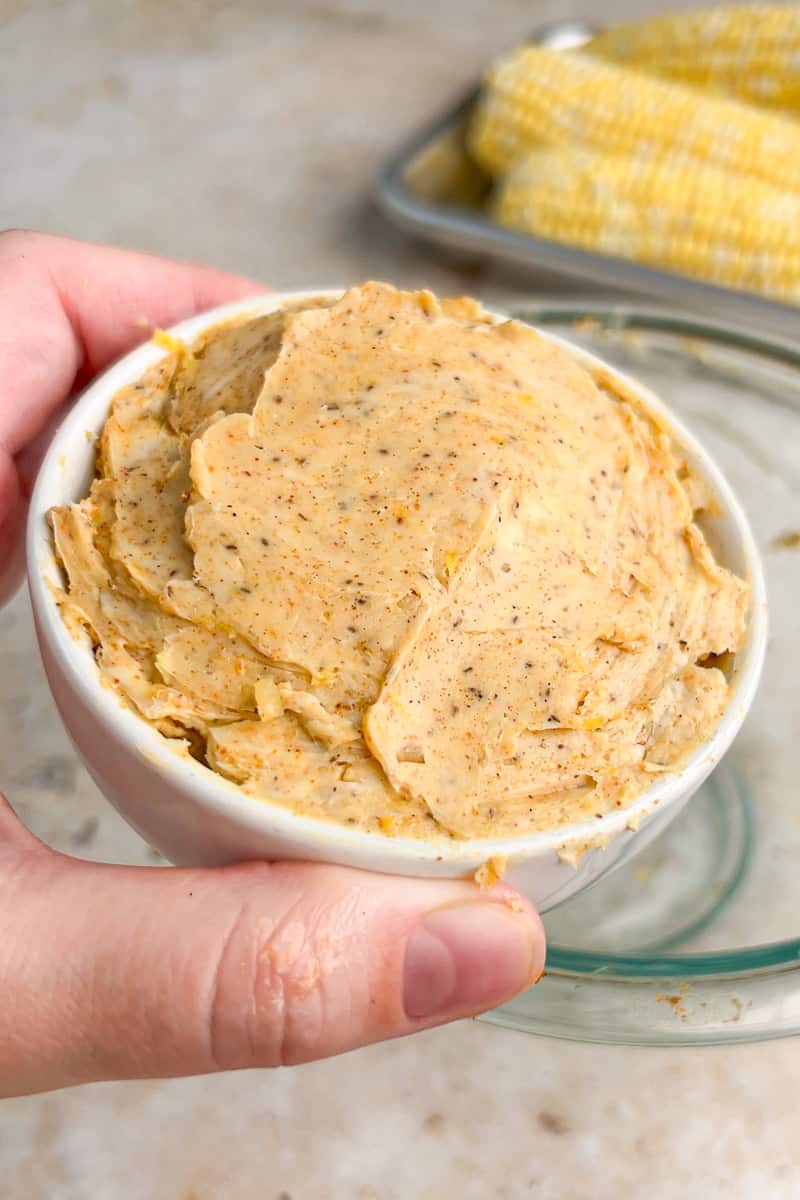 A hand holds a small bowl filled with creamy Old Bay butter.