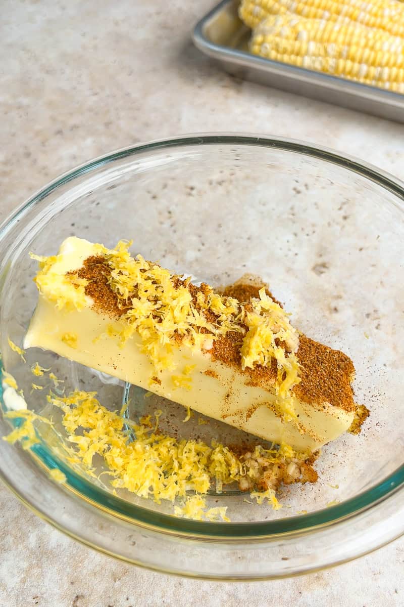 Softened butter, Old Bay seasoning, garlic, and lemon zest are added to a glass mixing bowl.