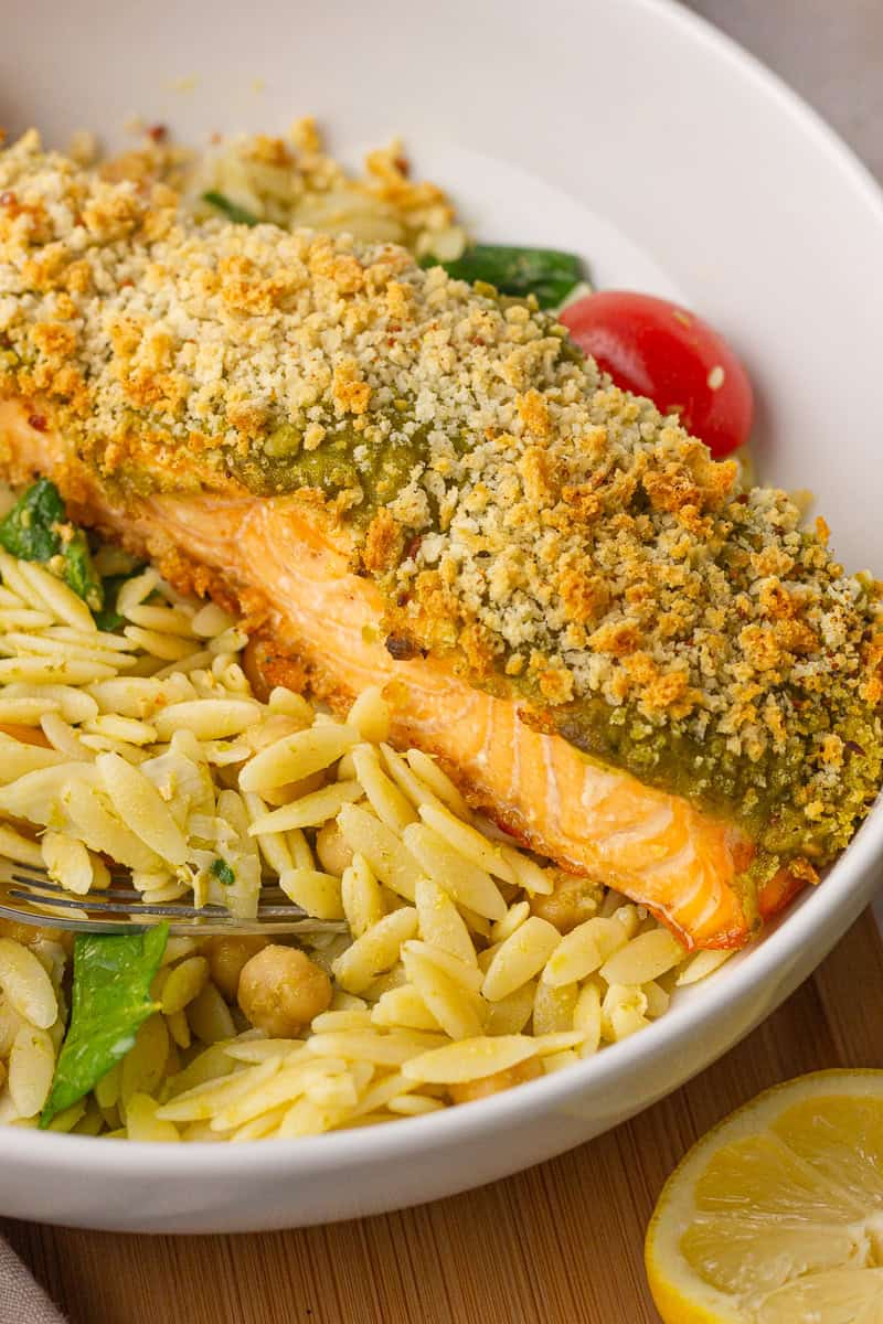 Cooked pesto crusted salmon is served over orzo with chickpeas, spinach, and tomatoes.