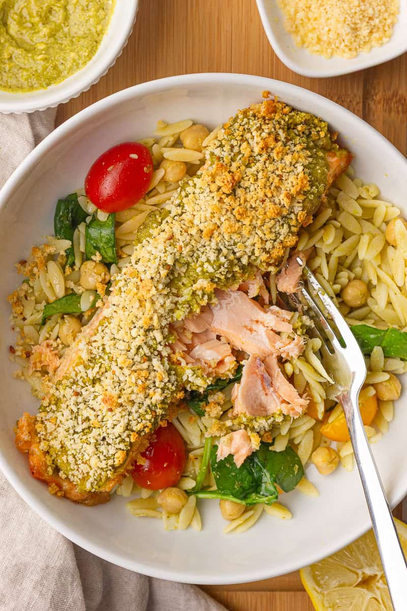 A fork breaks into the crispy pesto crusted salmon served over a fresh orzo salad.