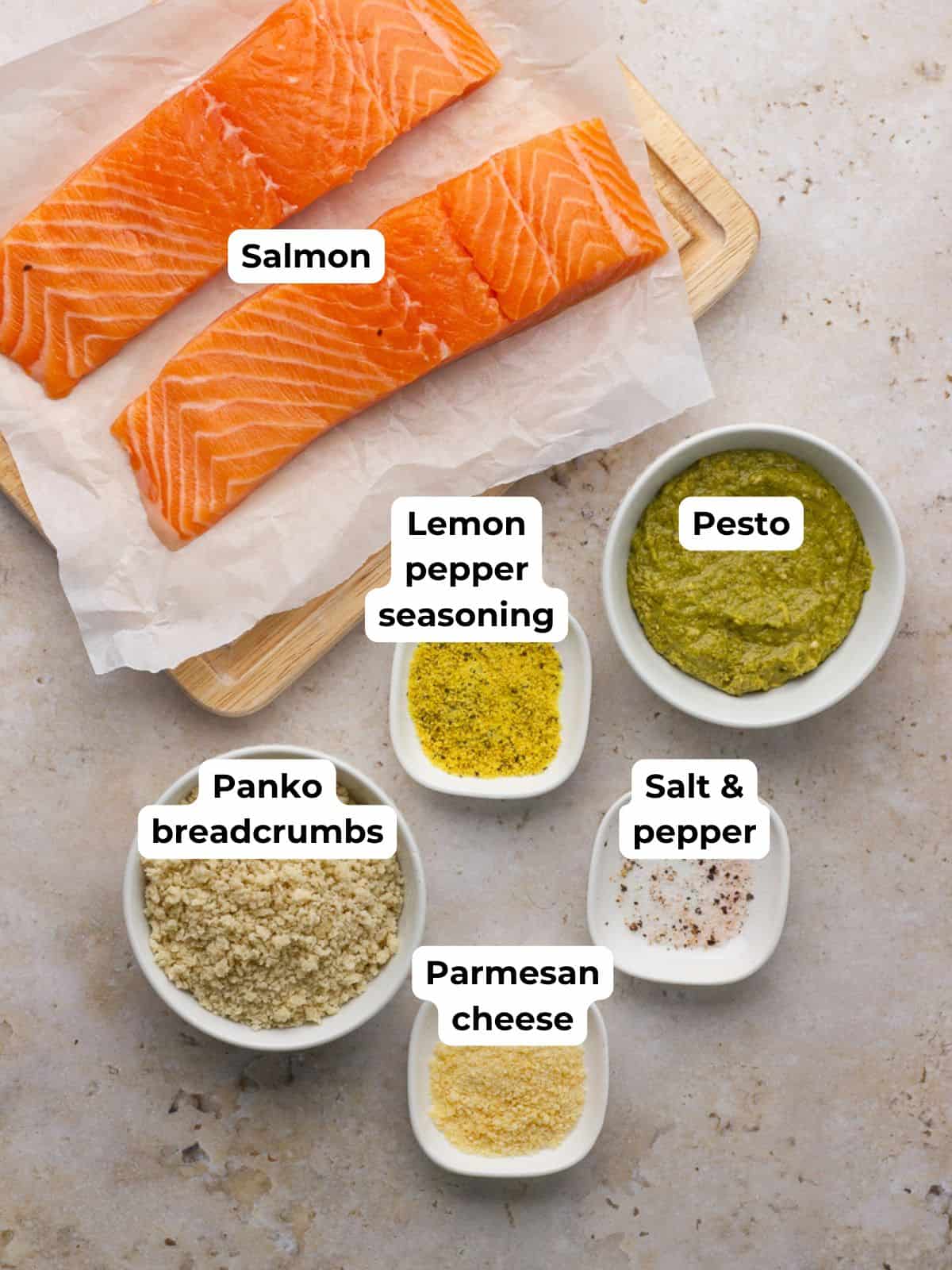 Simple ingredients for pesto crusted salmon are laid out including salmon, pesto, panko, parmesan, and seasoning.