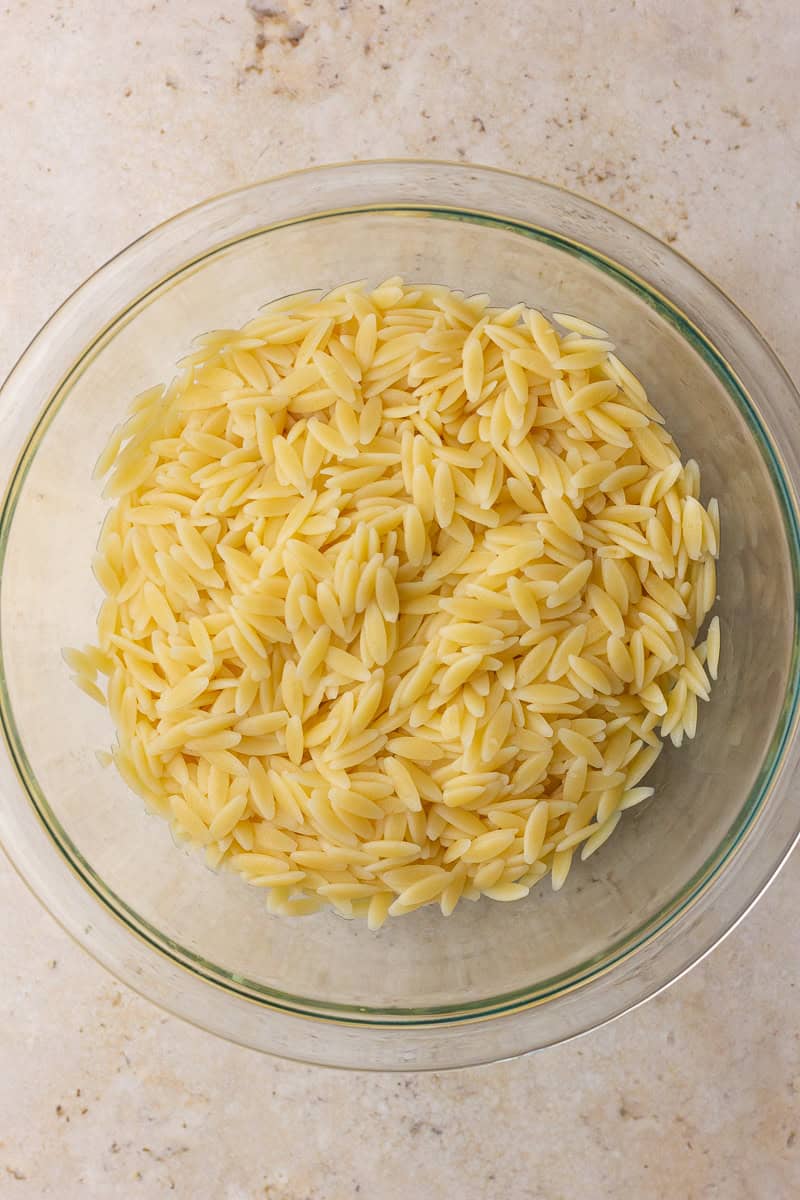 Cooked orzo sits in a glass bowl, ready to be tossed into this easy pesto orzo salad.