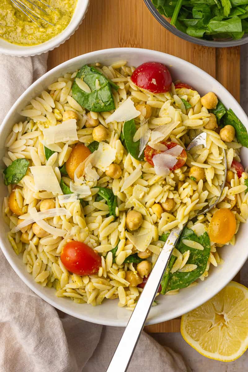 A bowl of pesto orzo salad is tossed together with chickpeas, spinach, and juicy tomatoes.