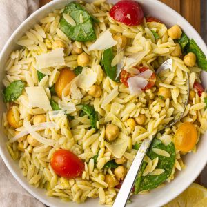 A fresh bowl of pesto orzo salad served with chickpeas, spinach, tomatoes, and parmesan.