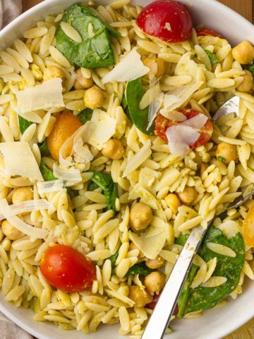 A fresh bowl of pesto orzo salad served with chickpeas, spinach, tomatoes, and parmesan.