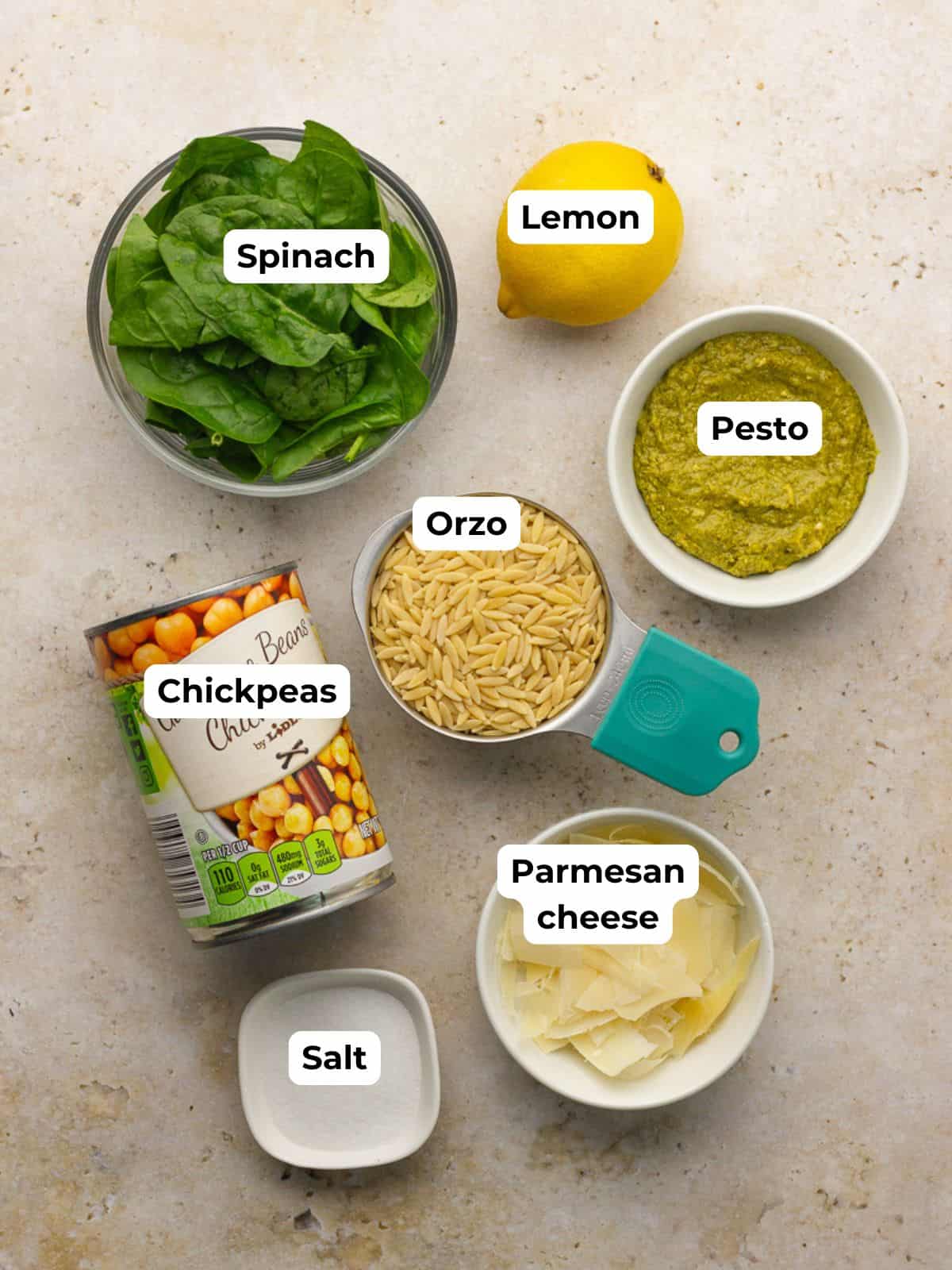 Ingredients for pesto orzo salad including orzo, pesto, chickpeas, spinach, lemon, and parmesan.
