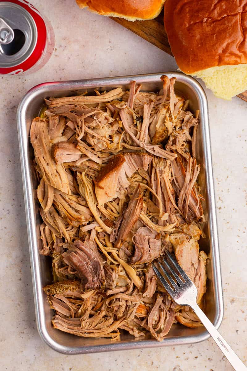 Shredded pulled pork is served in a metal pan with buns and Coke nearby.