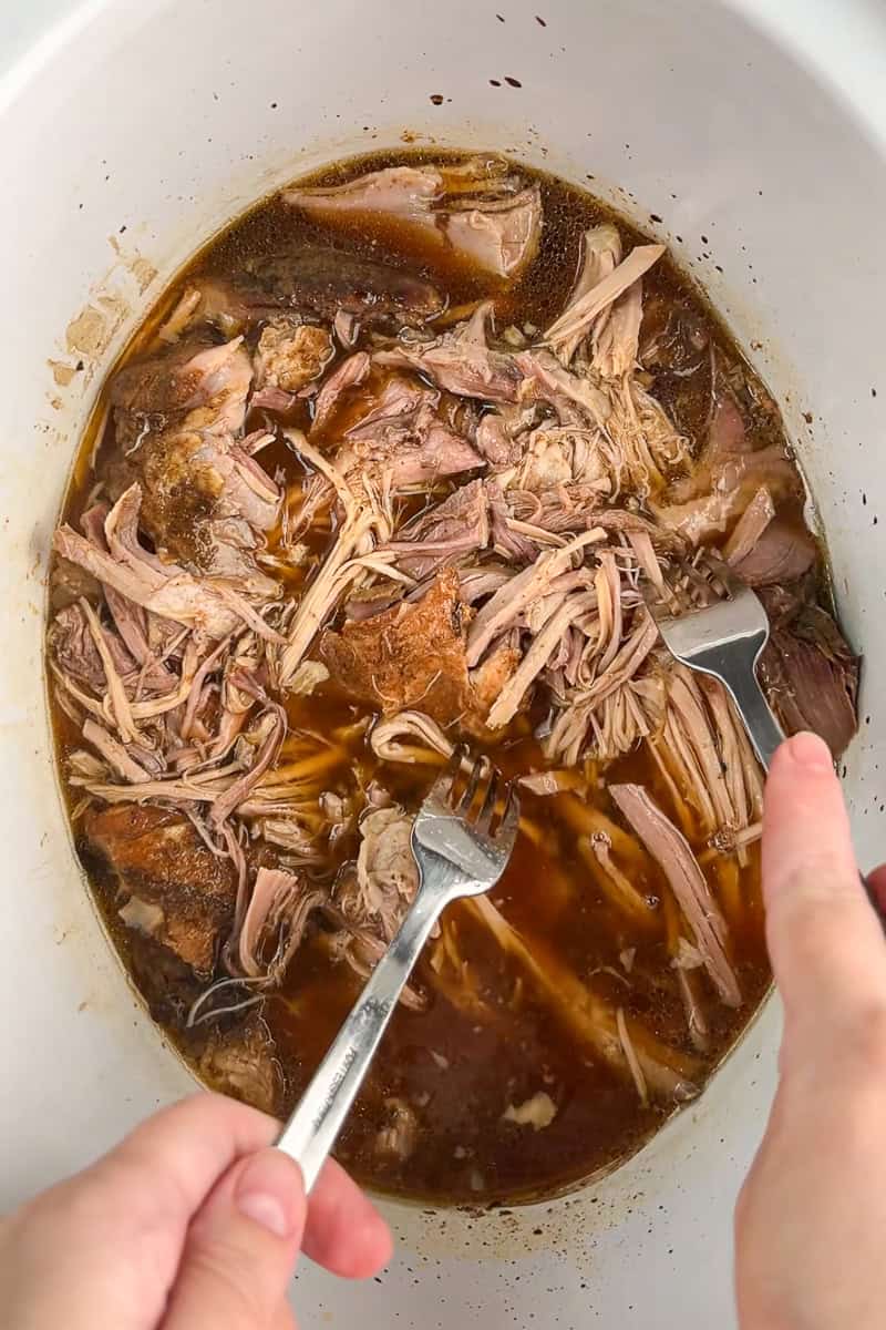 Pulled pork is shredded with two forks in a slow cooker.