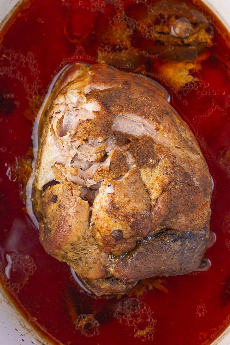 Cooked pork shoulder sits in a slow cooker with Coke cooking liquid.