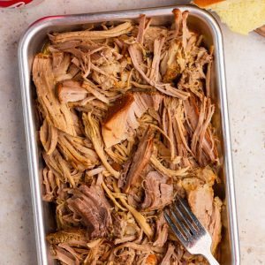 Shredded pulled pork is served in a metal pan with buns on the side.