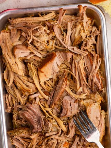 Shredded pulled pork is served in a metal pan with buns on the side.