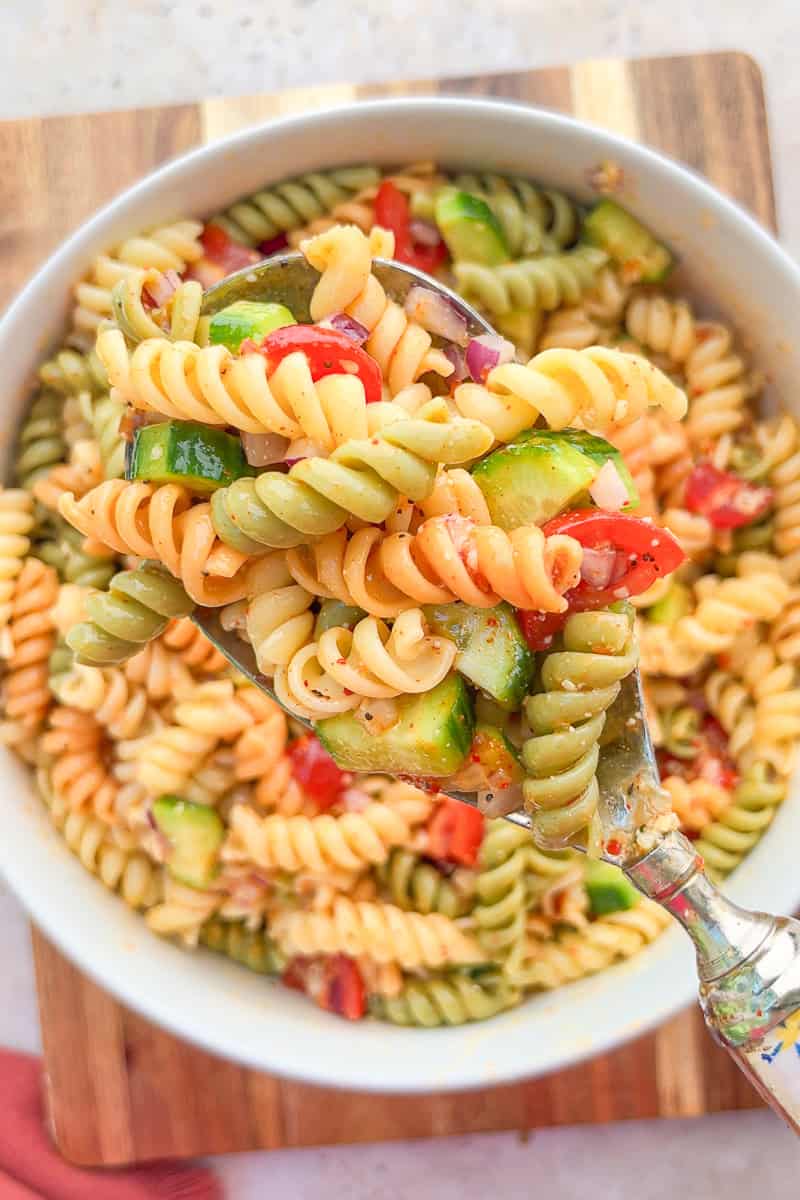 A serving spoon lifts salad supreme pasta salad from a white bowl.
