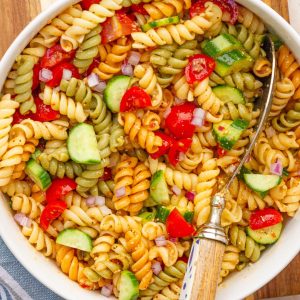 A bowl of colorful salad supreme pasta salad is served with a large spoon.
