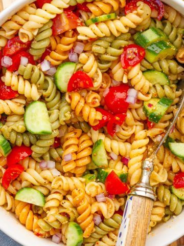 A bowl of colorful salad supreme pasta salad is served with a large spoon.