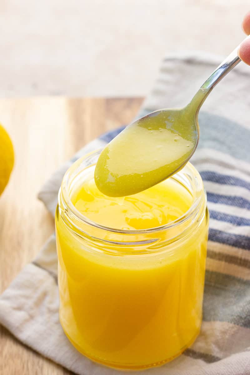 A spoon lifts silky homemade lemon curd from a small glass jar.