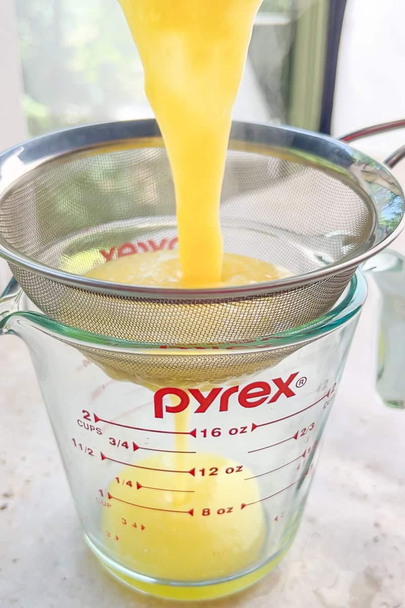 Fresh lemon curd pours through a fine mesh strainer into a glass measuring cup.