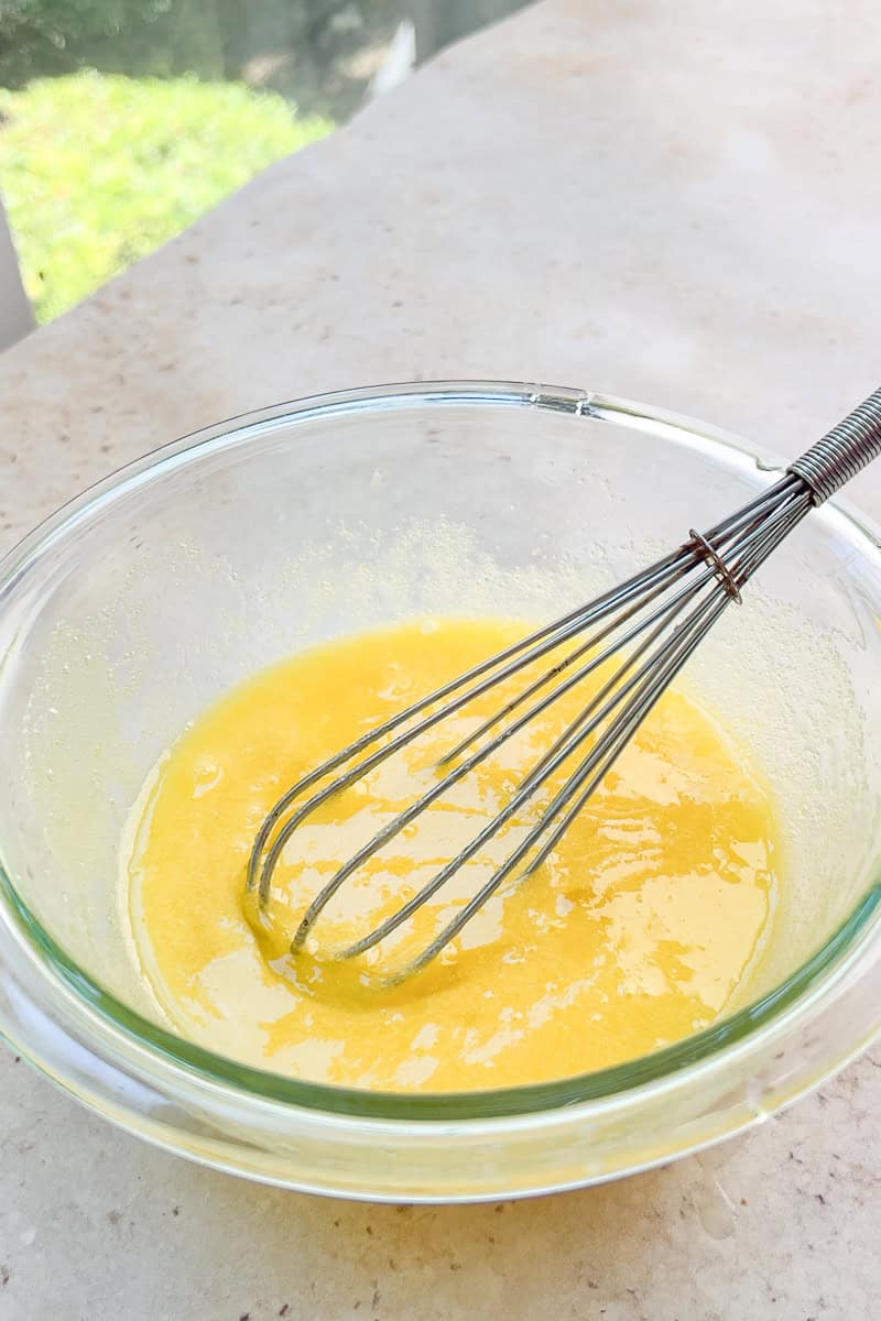 A whisk mixes the egg and sugar mixture for homemade lemon curd in a glass bowl.