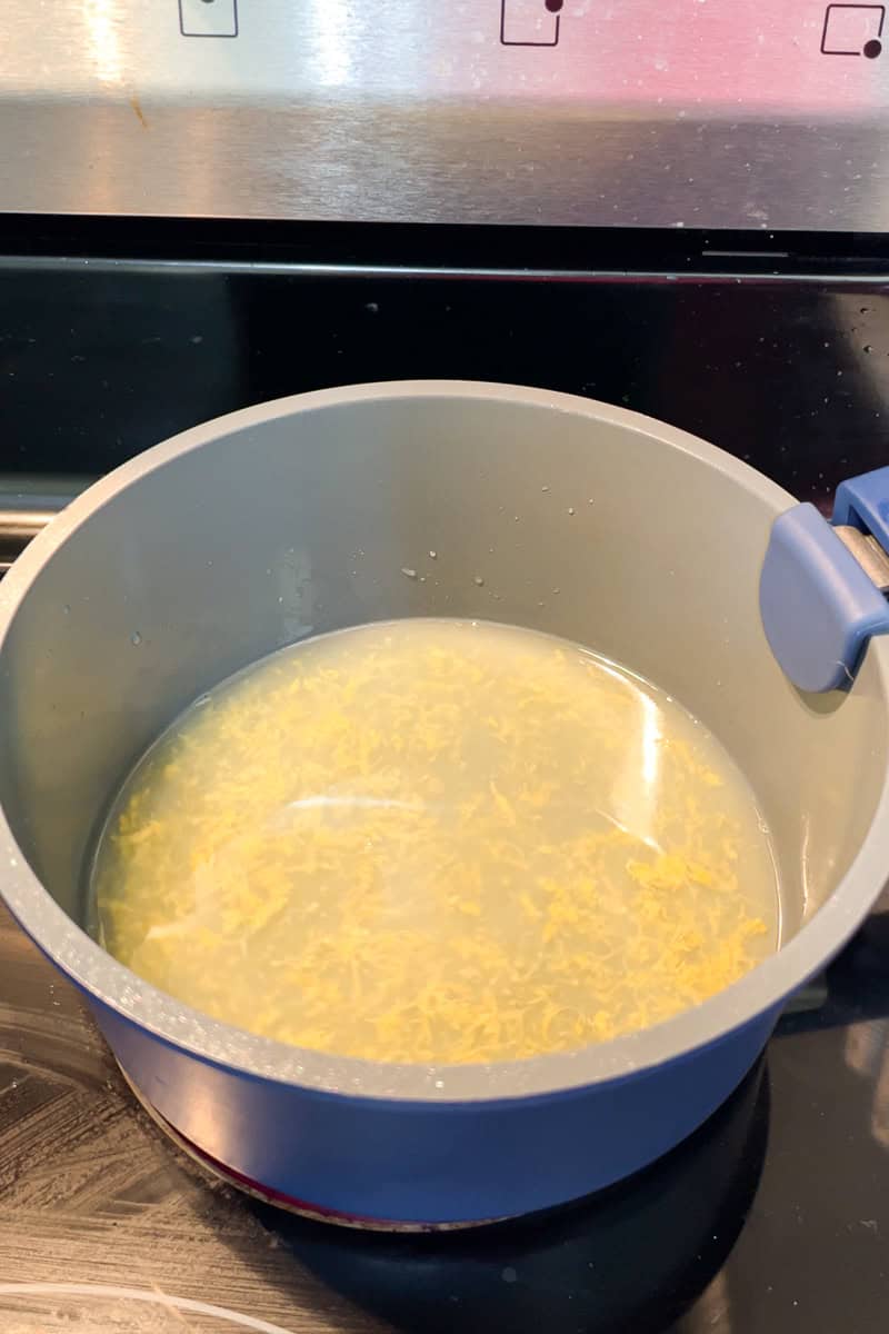 Lemon juice and fresh lemon zest heat together in a saucepan on the stove.