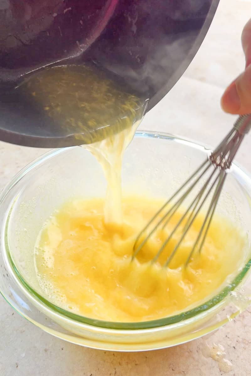 Hot lemon juice pours into the egg mixture while a whisk blends everything together.