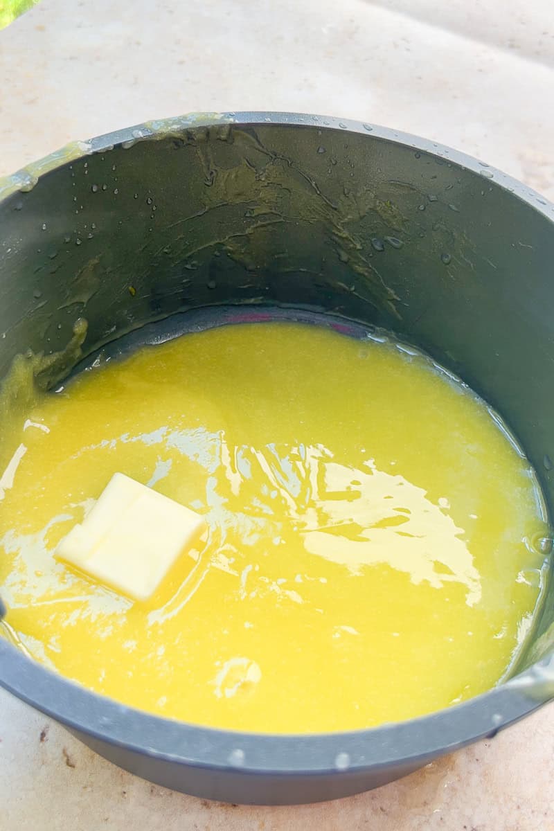 Butter melts into warm homemade lemon curd inside a saucepan.