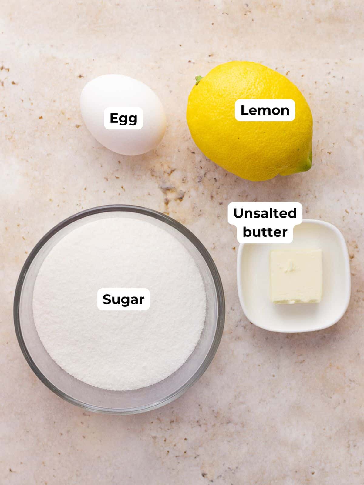 Fresh lemon curd ingredients including lemon, egg, sugar, and butter sit on a countertop.