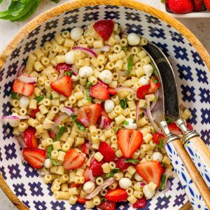 Strawberry pasta salad with mozzarella pearls, basil, red onion, and balsamic dressing sits tossed together in a large serving bowl.
