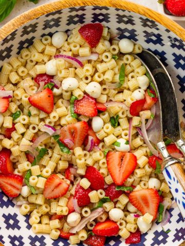Strawberry pasta salad with mozzarella pearls, basil, red onion, and balsamic dressing sits tossed together in a large serving bowl.