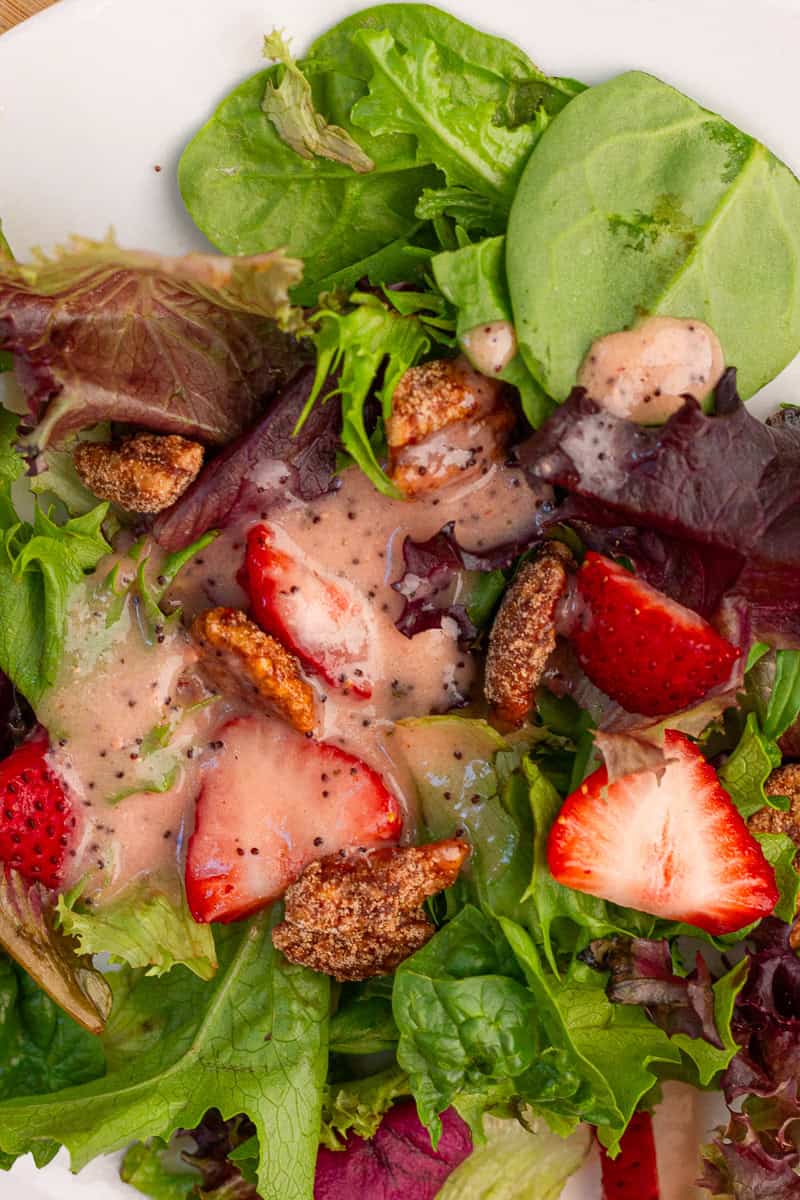 A strawberry salad with mixed greens, candied pecans, and creamy strawberry poppyseed dressing fills a white plate.