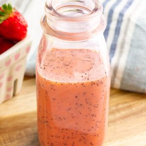 A close-up jar of strawberry poppyseed dressing shows its creamy pink texture and poppy seeds.