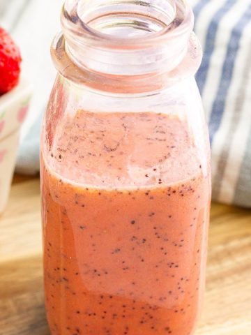 A close-up jar of strawberry poppyseed dressing shows its creamy pink texture and poppy seeds.