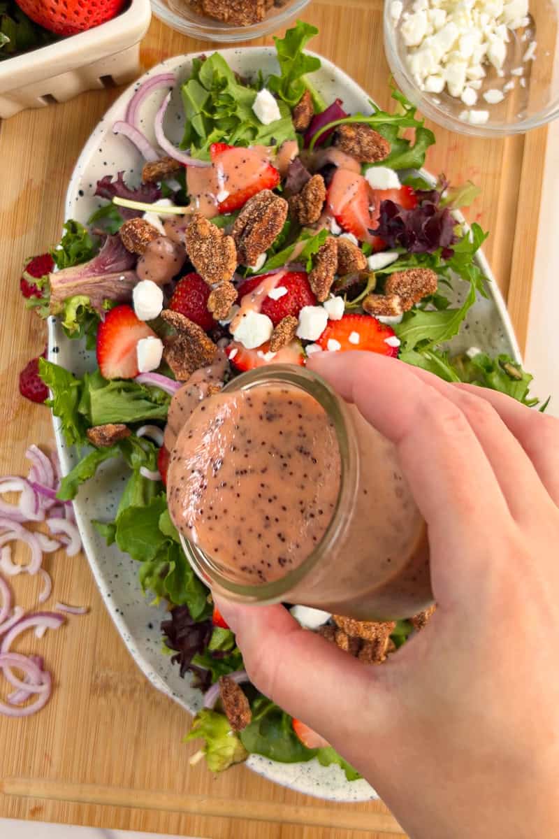 Strawberry poppyseed dressing is poured over a strawberry goat cheese salad.
