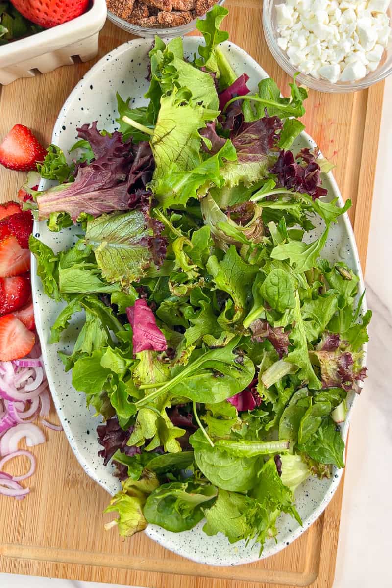 Mixed greens are layered on a platter to start the strawberry goat cheese salad.