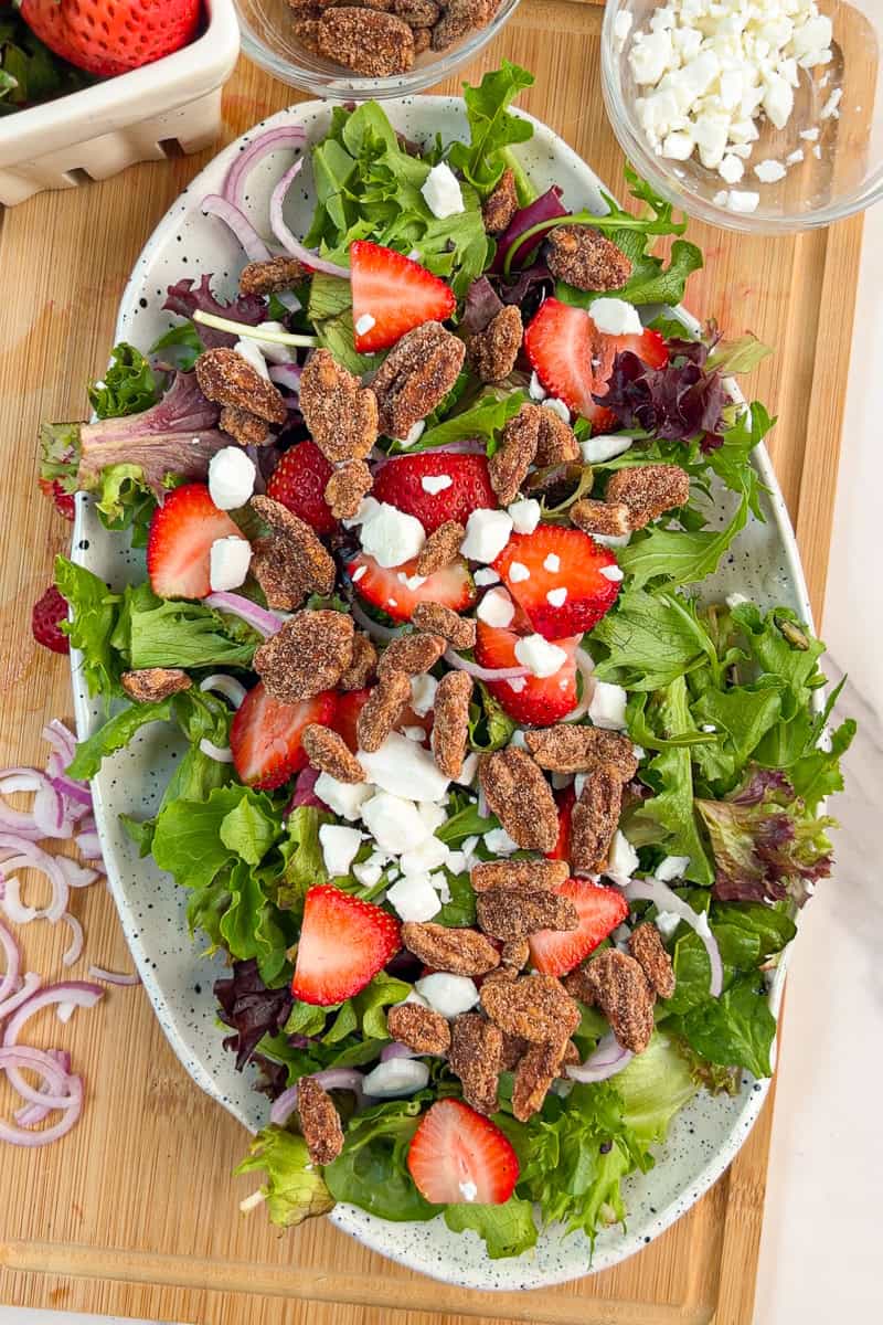 Strawberries, goat cheese, red onion, and cinnamon pecans are arranged over mixed greens.