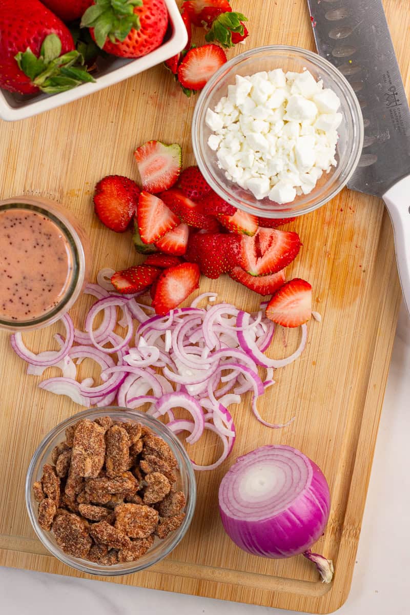 Ingredients for strawberry salad with goat cheese are arranged on a cutting board.