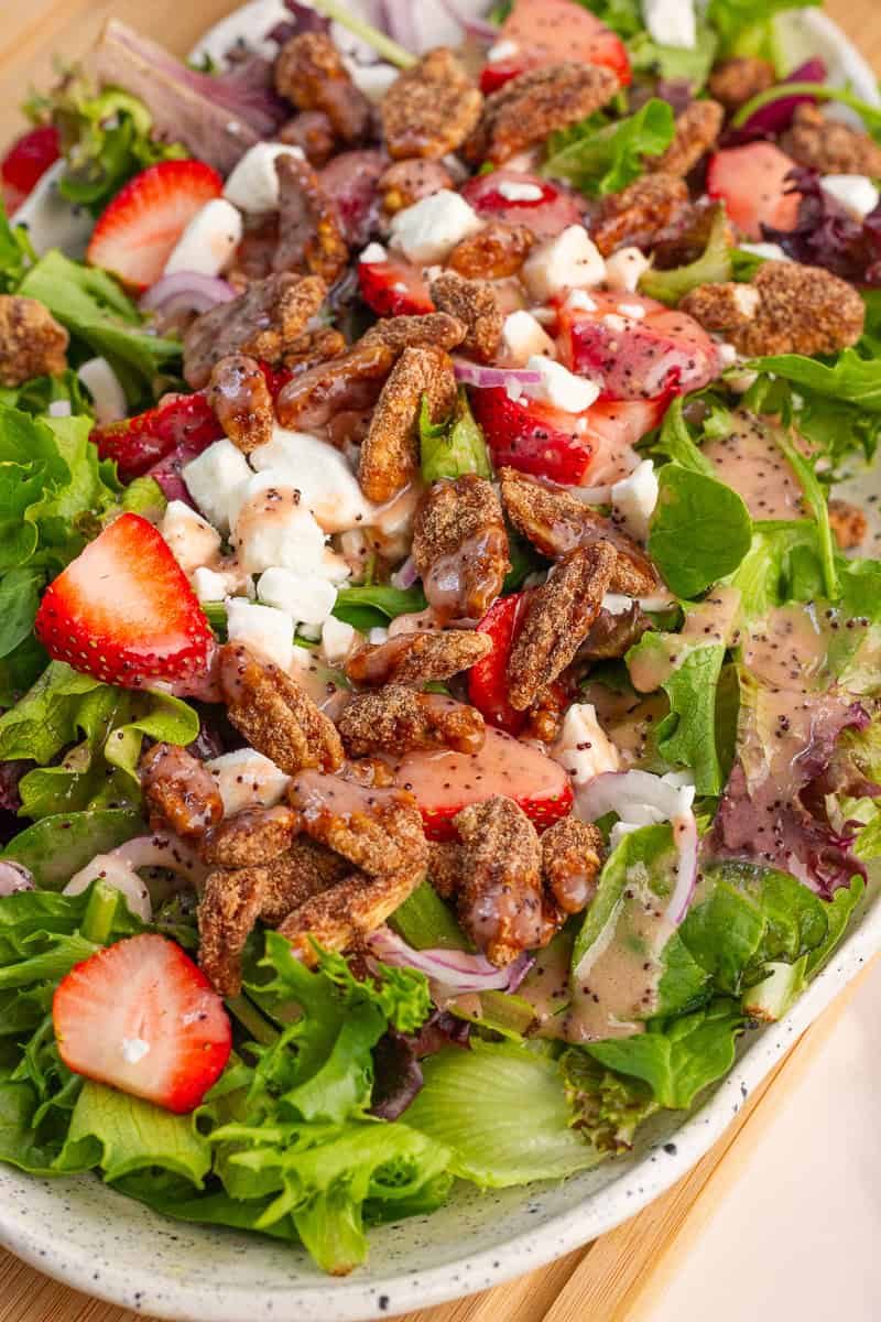 A close-up shows strawberry salad with goat cheese, cinnamon pecans, and strawberry poppyseed dressing.