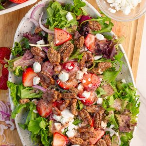 A finished strawberry salad with goat cheese, cinnamon pecans, and strawberry poppyseed dressing fills a serving platter.