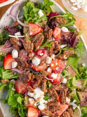 A finished strawberry salad with goat cheese, cinnamon pecans, and strawberry poppyseed dressing fills a serving platter.