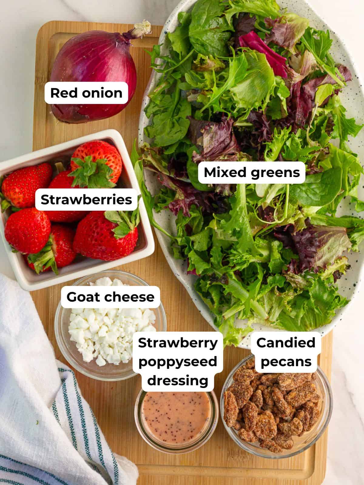 Labeled ingredients for strawberry salad with goat cheese are shown on a cutting board.