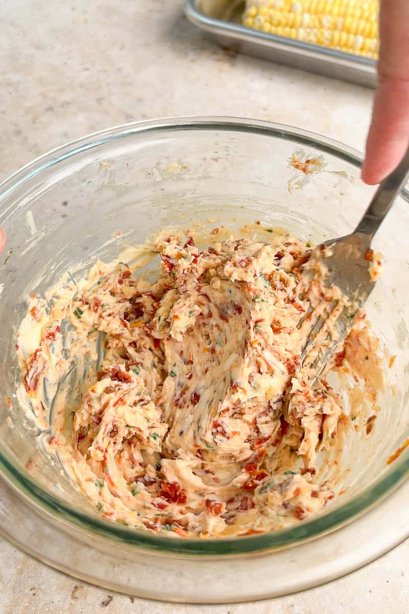 Tomato basil butter is mixed together in a glass bowl with a fork.
