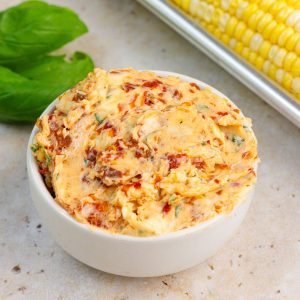 Tomato basil butter is served in a white bowl with fresh basil and corn on the cob.