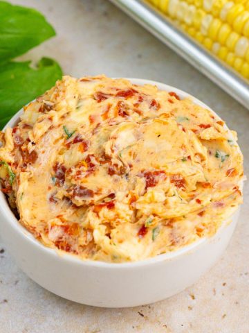 Tomato basil butter is served in a white bowl with fresh basil and corn on the cob.