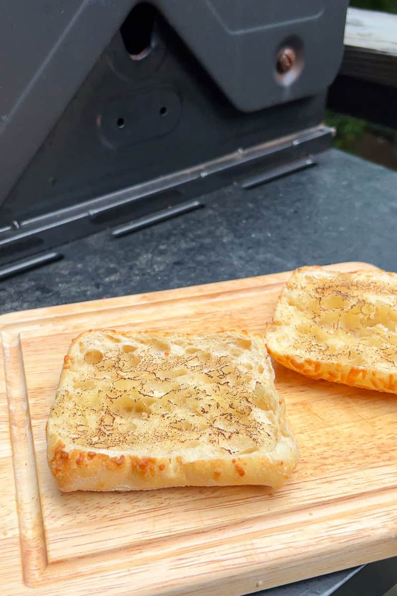 Toasted ciabatta rolls sit open on a wooden cutting board, ready to be assembled into chicken Caprese sandwiches.