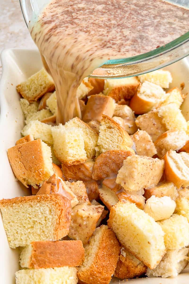 Cinnamon custard is poured over cubed brioche in a baking dish for peach French toast casserole.