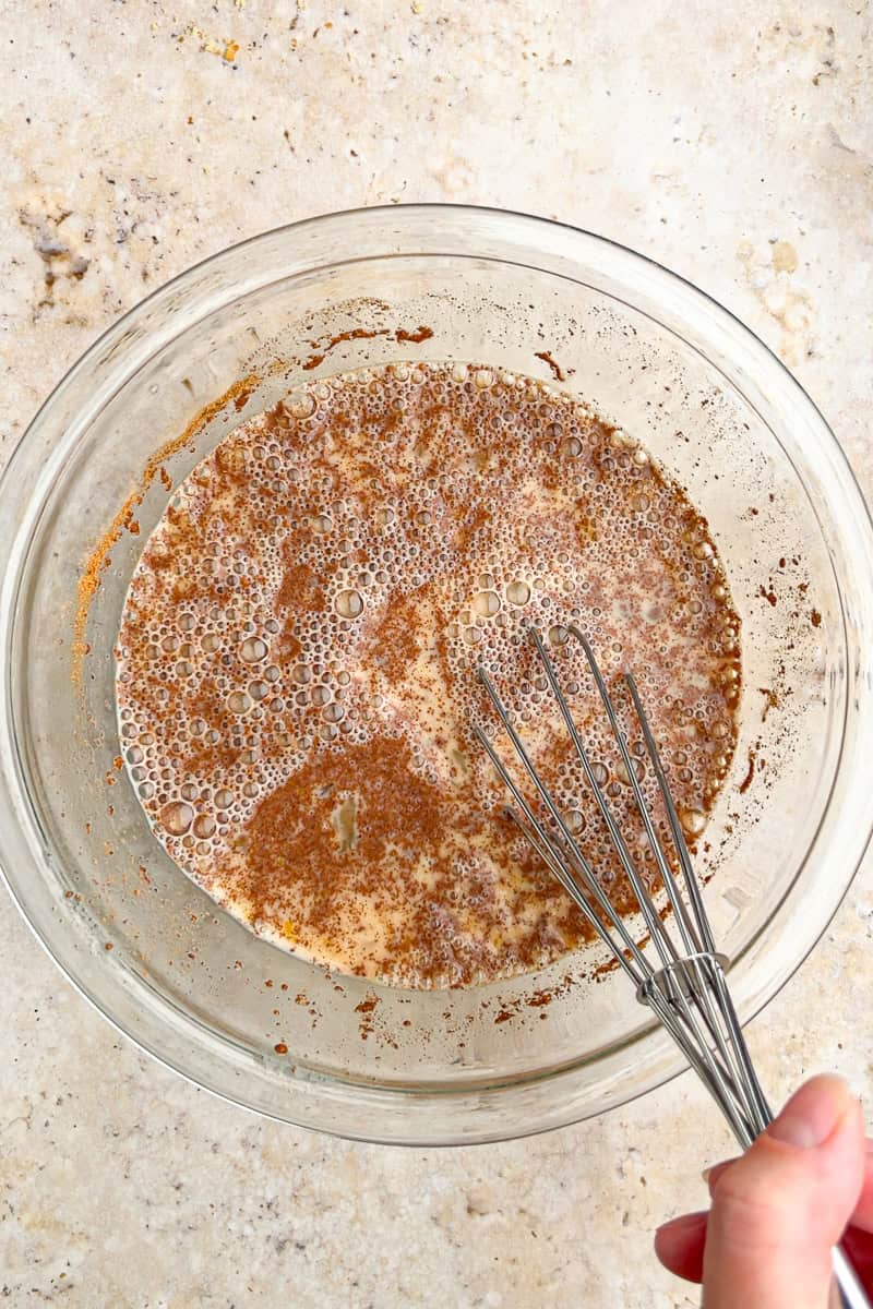 A whisk stirs together the cinnamon-spiced custard mixture for peach French toast casserole.