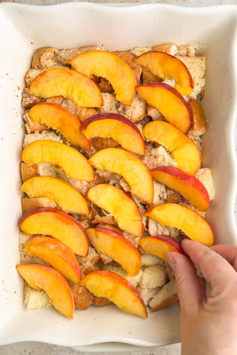 Fresh peach slices are arranged over the bread mixture in the baking dish for peach French toast casserole.