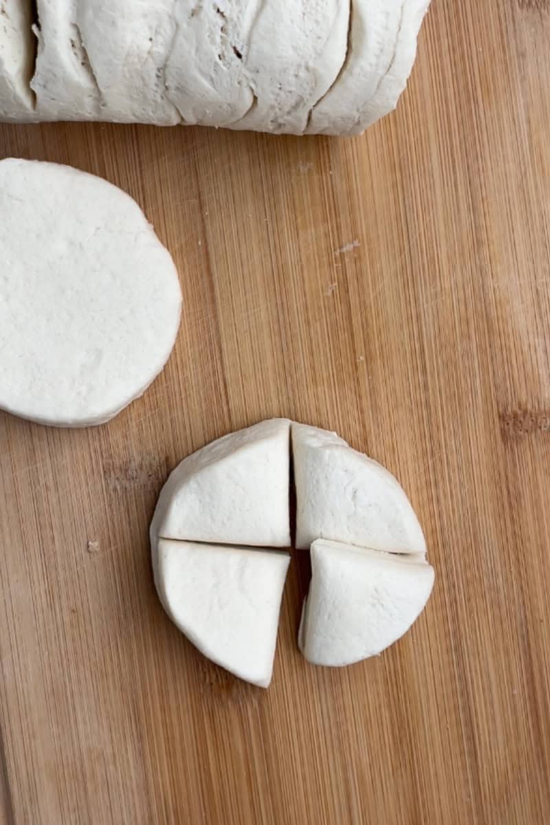 Refrigerated biscuit dough is cut into four pieces on a wooden cutting board.