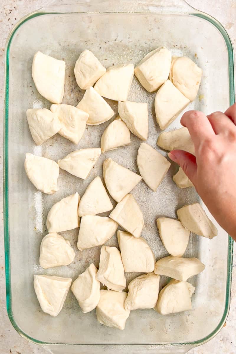 Cut biscuit pieces are arranged in a greased baking dish for biscuit pizza casserole.