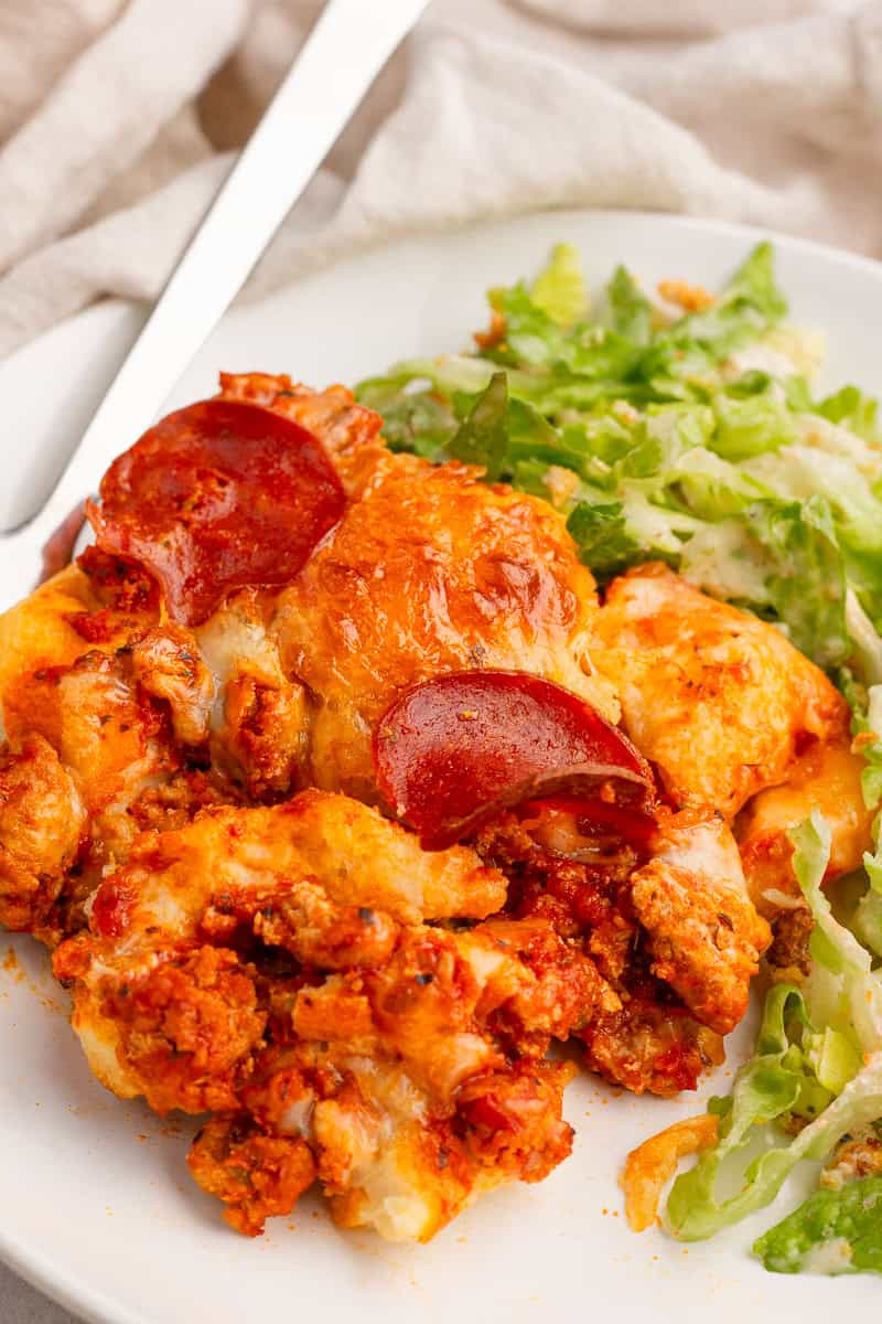 A serving of biscuit pizza casserole is plated with a Caesar salad on the side.